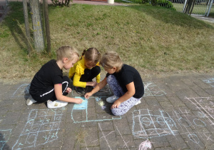 trzy dziewczynki rysują kredą po chodniku wzorki